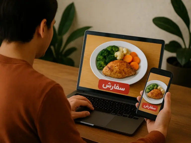 تصویری از فردی که با لپ‌تاپ و موبایل در حال ثبت سفارش غذای شرکتی است